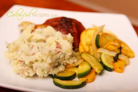 Red garlic dill mashed potatoes on a plate with chicken and sautéed squash