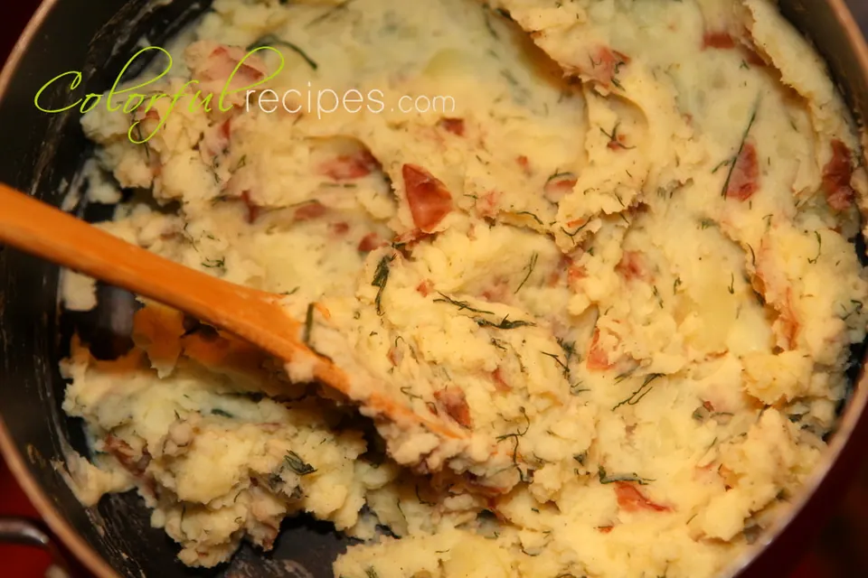 Pot of skin-on red garlic dill mashed potatoes with a wooden spoon
