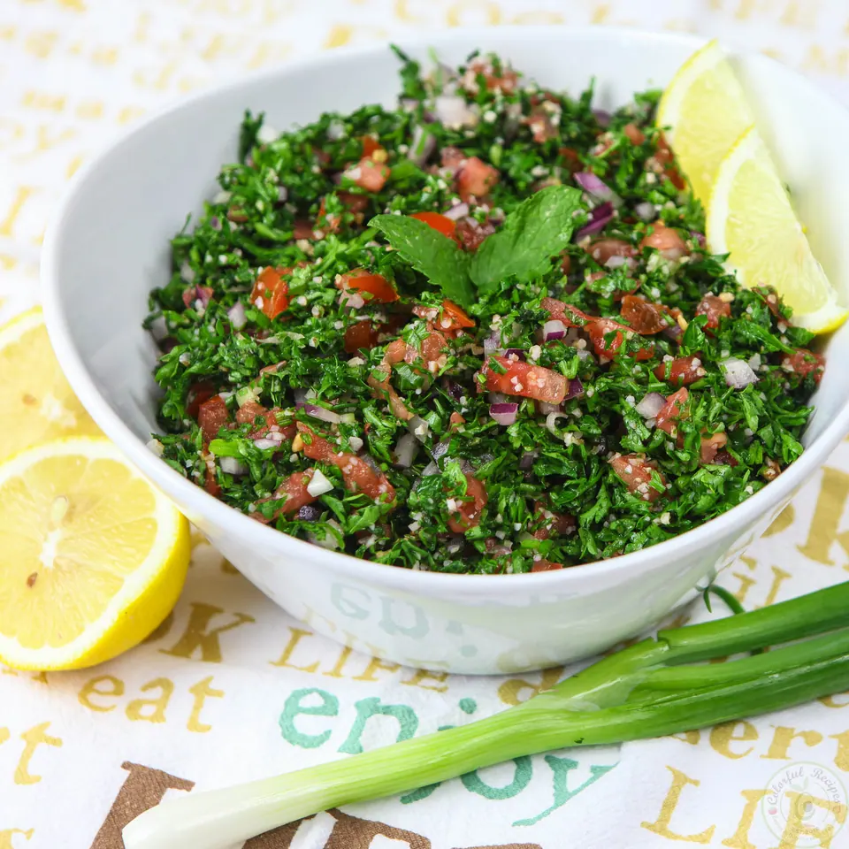 Authentic Lebanese tabbouleh in a white bowl with lemon wedges and green onion