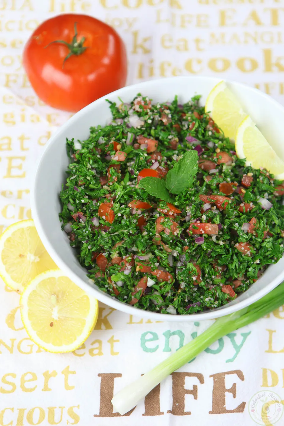 Bowl of fresh and light authentic Lebanese tabbouleh next to a whole tomato and lemons