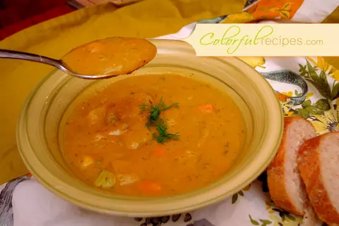 Bowl of carrot potato zucchini soup garnished with fresh dill, served with bread