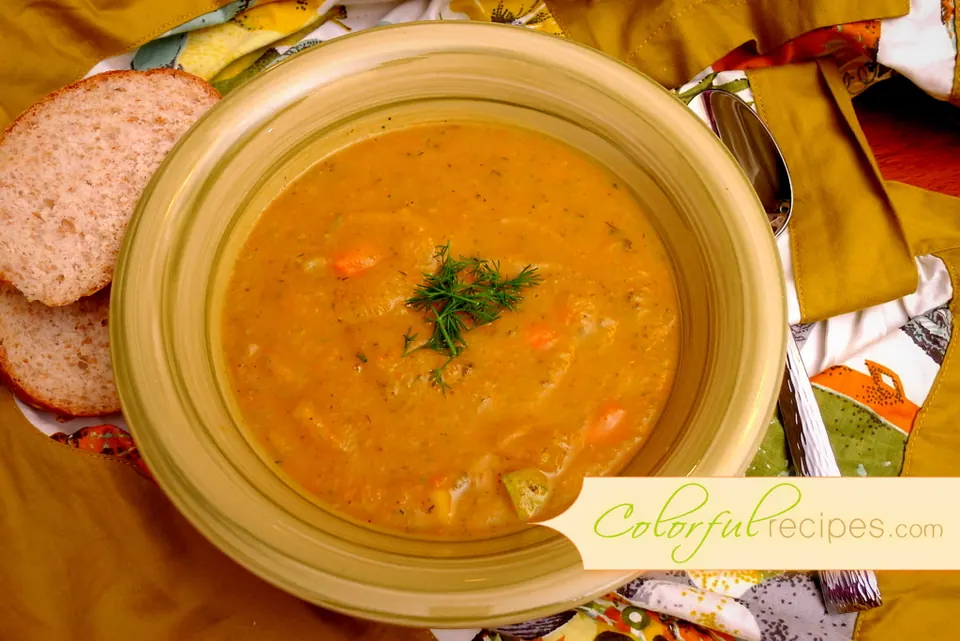 Bowl of carrot potato zucchini soup garnished with fresh dill, served with bread