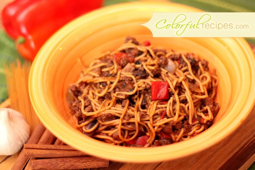 Mom's comfort spaghetti in an orange bowl with red bell pepper and garlic