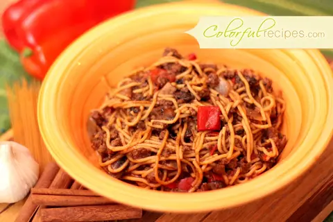 Mom's comfort spaghetti in an orange bowl with red bell pepper and garlic