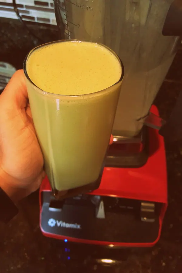 Glass of heart-healthy green smoothie with cashews in front of a Vitamix blender