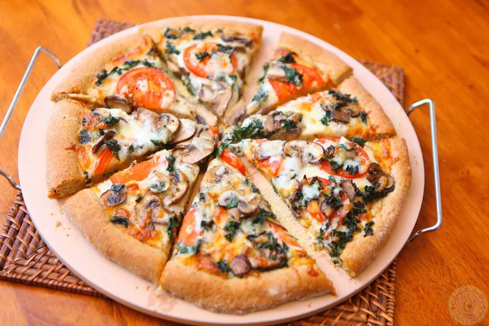 Sliced flax whole wheat kale pizza with mushrooms and tomatoes on a pizza stone
