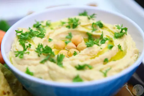 Bowl of 5 minute creamy hummus garnished with chickpeas, olive oil and parsley