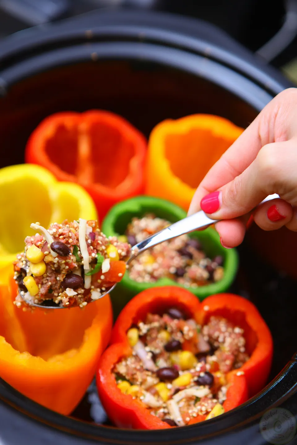 Spooning quinoa and beef filling into bell peppers in a crockpot