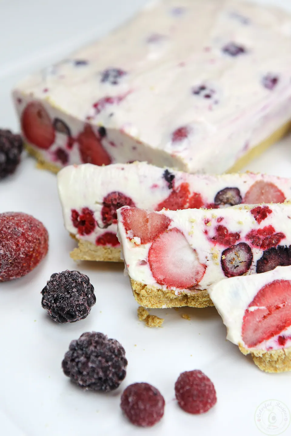 Slices of no bake frozen berry cheesecake with strawberries and blackberries on a graham cracker crust