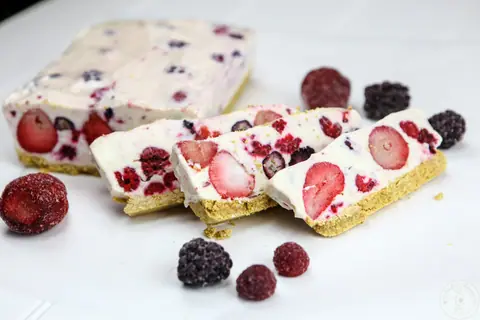 Slices of no bake frozen berry cheesecake with frozen berries on a graham cracker crust
