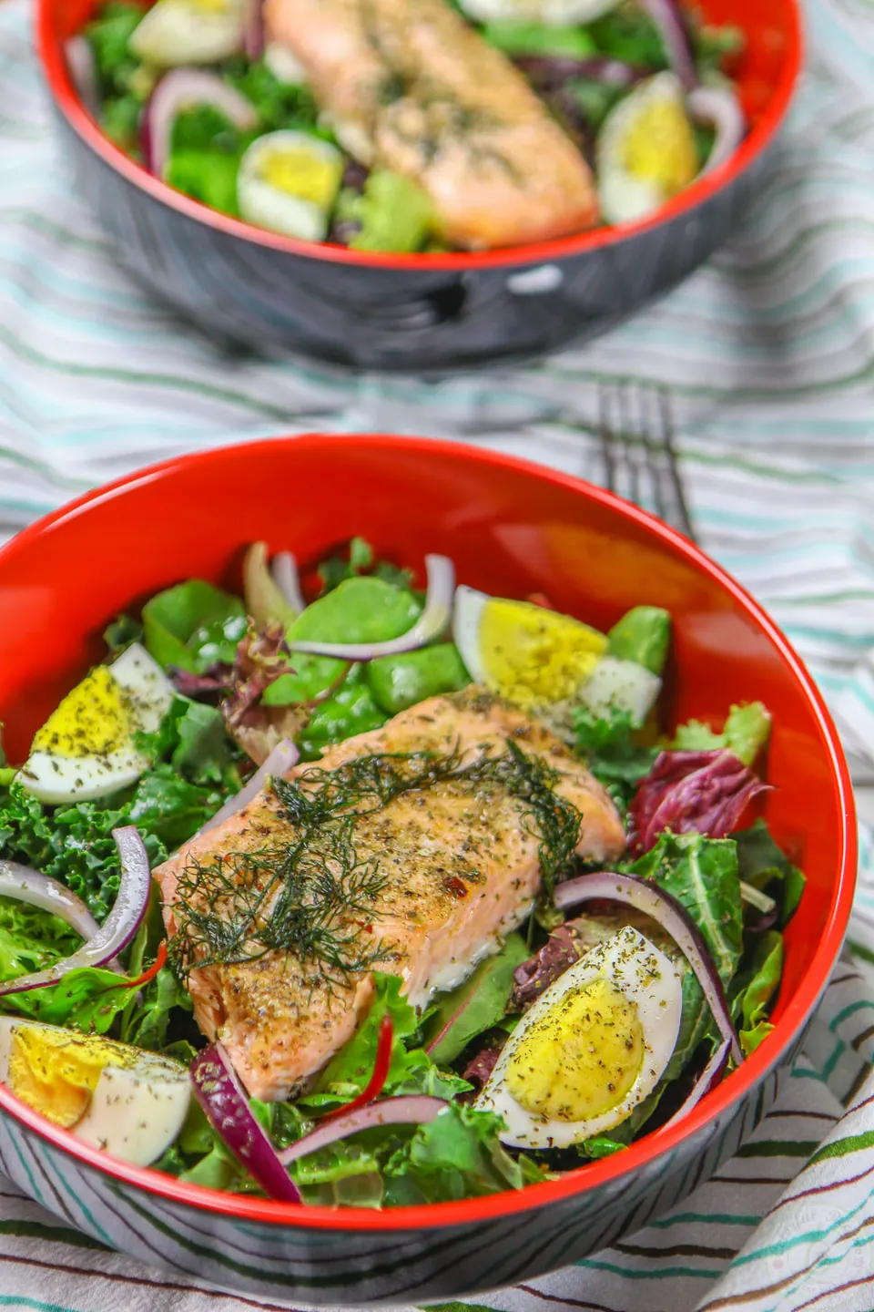 Quick leftover salmon salad with boiled eggs, red onion and greens in red bowls