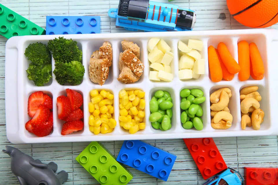 Toddler approved ice cube tray colorful buffet with broccoli, strawberries, corn, edamame, carrots and cashews