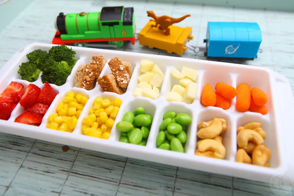 Toddler ice cube tray buffet with strawberries, corn, edamame, bread and cheese