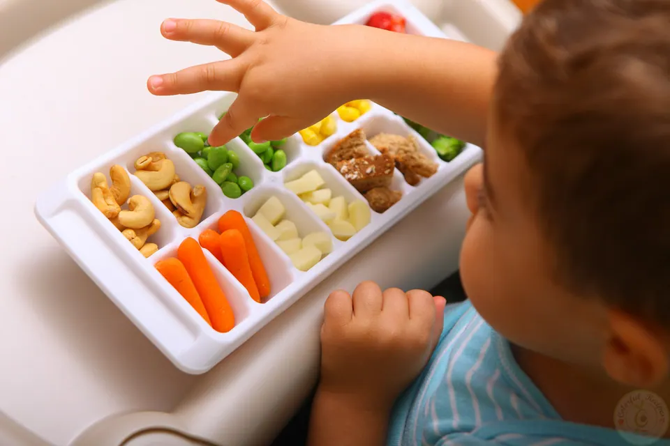 Toddler reaching for snacks in an ice cube tray colorful buffet