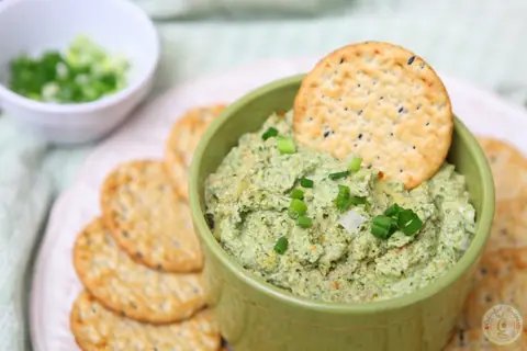 Hot and hearty artichoke spinach dip in a casserole dish with multigrain crackers