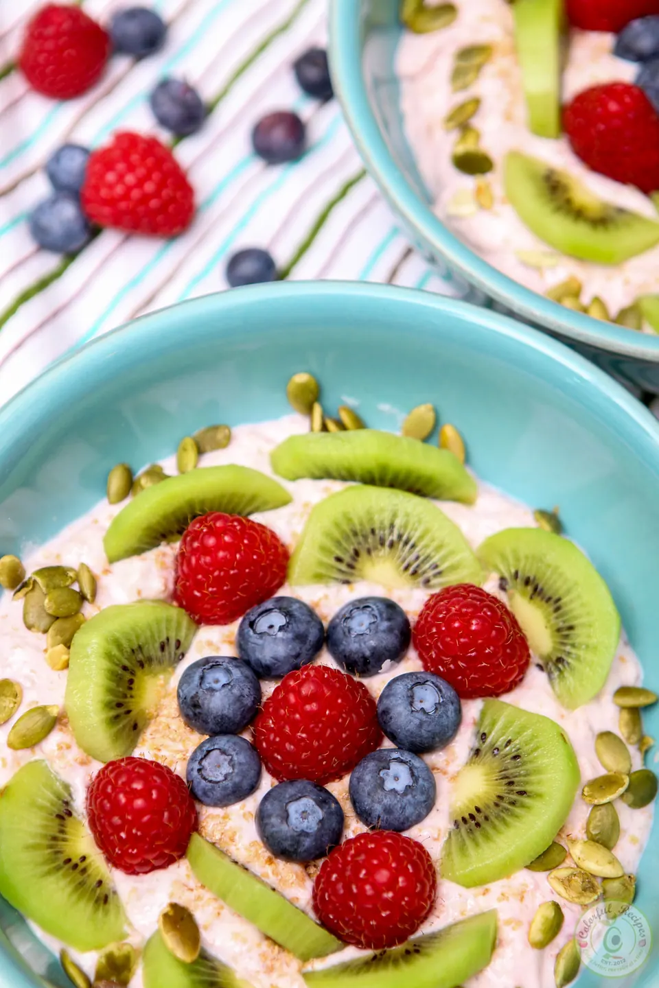 Banana yogurt fruit breakfast bowl topped with kiwi, raspberries, blueberries and pumpkin seeds