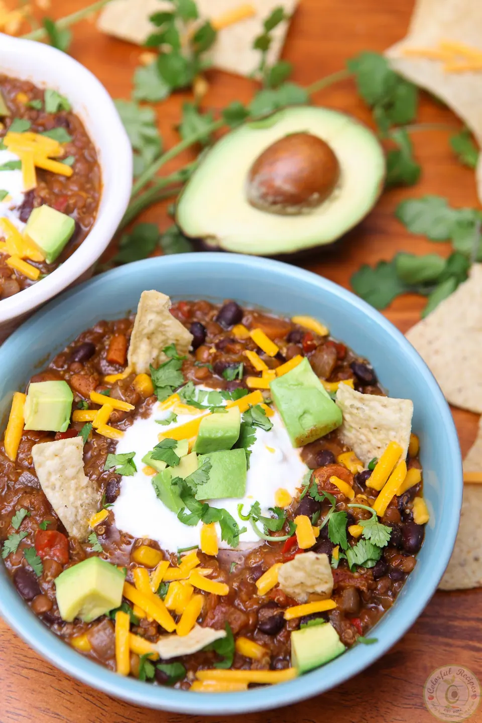 Bowl of crock pot black bean lentil quinoa chili topped with Greek yogurt, cheddar, avocado and tortilla chips