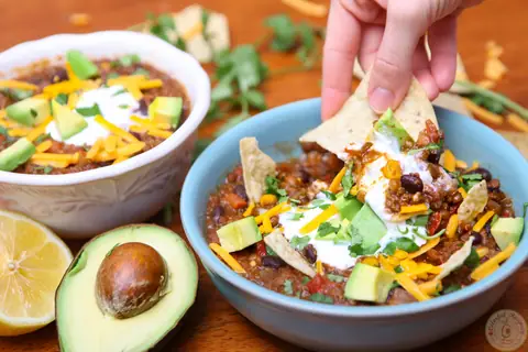 Bowl of crock pot black bean lentil quinoa chili topped with avocado, cheddar and tortilla chips