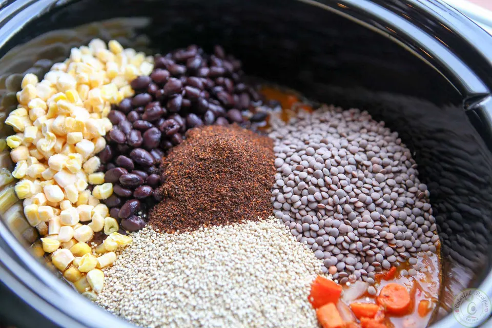 Corn, black beans, lentils, quinoa and chili powder in a Crock Pot before stirring
