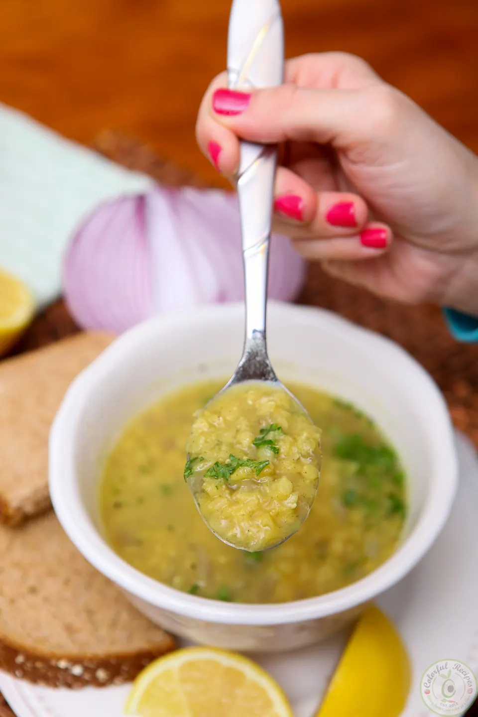Spoon lifting red lentil soup from a bowl with parsley and lemon