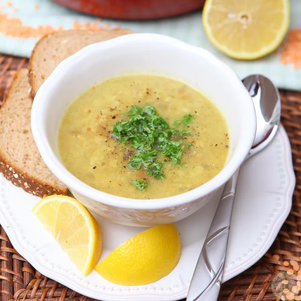 Shorbet Adas red lentil soup garnished with parsley, served with bread and lemon