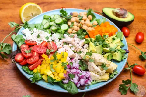 Colorful fresh chopped salad with chicken, chickpeas, avocado, feta and veggies arranged in sections