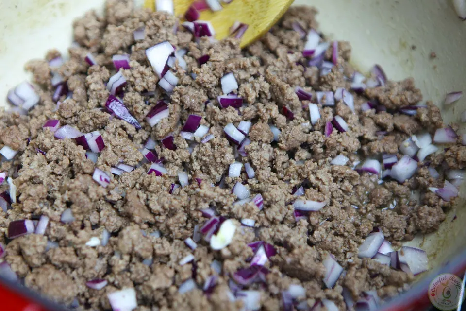 Ground beef browning with onion and cinnamon in a Dutch oven