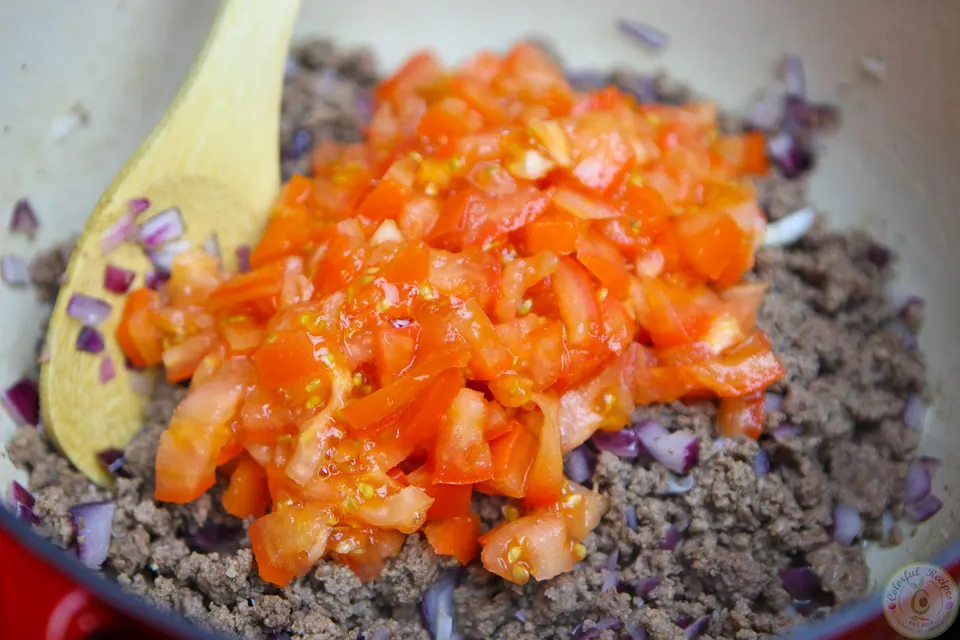 Chopped fresh tomatoes added to ground beef in a pot