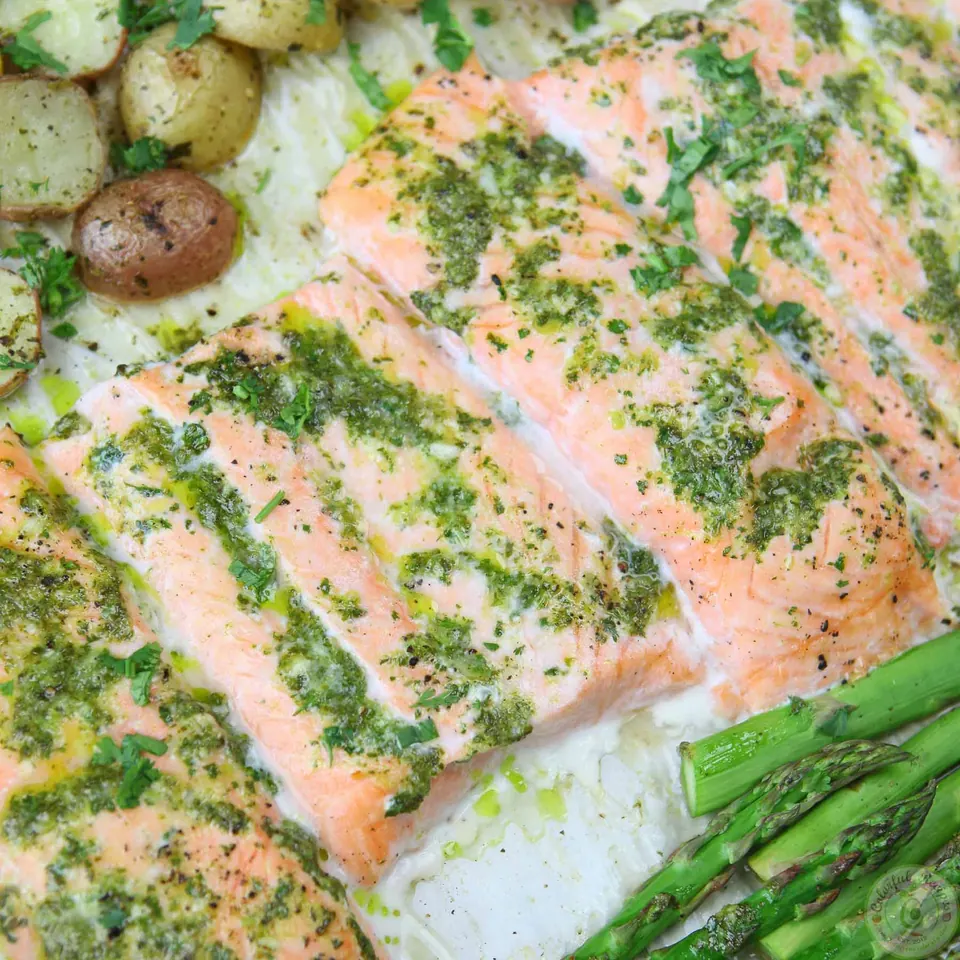 Close-up of salmon topped with cilantro garlic citrus butter next to asparagus and potatoes