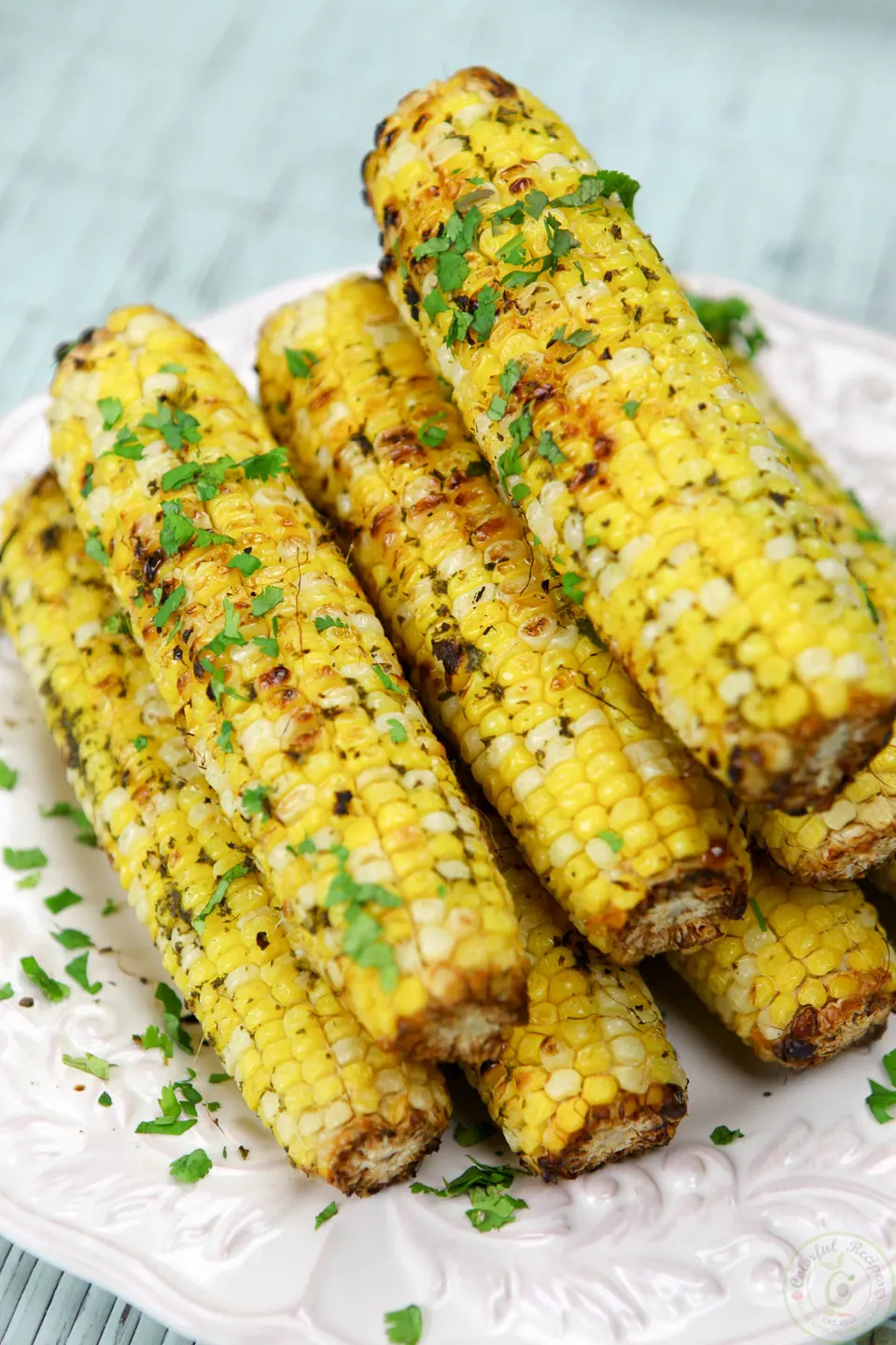 Charred ears of grilled corn on the cob with cilantro garlic citrus butter on a white plate