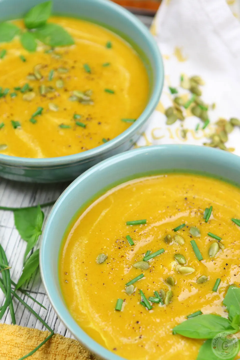 Two bowls of creamy butternut squash sweet potato soup garnished with green onions and pepitas