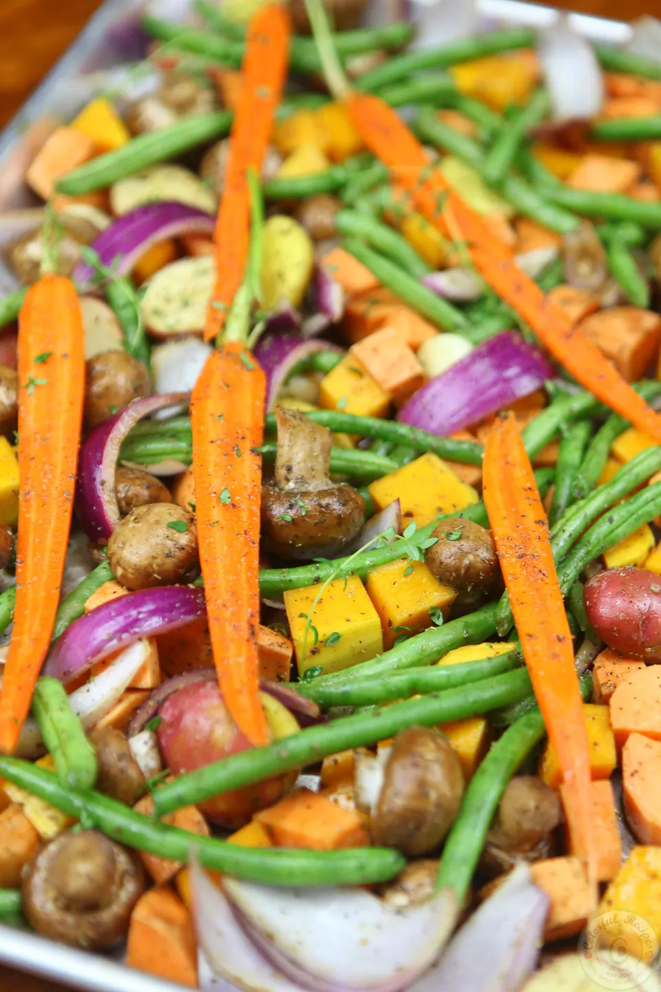 Roasted fall vegetables with carrots, green beans and red onion on a baking sheet