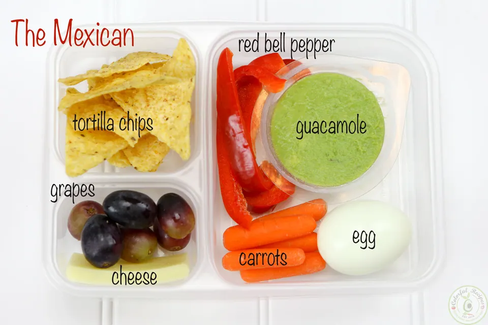 The Mexican protein bento snack box with guacamole, egg, carrots, red bell pepper, tortilla chips, grapes and cheese