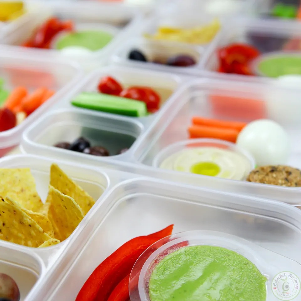 Close-up of colorful protein bento snack boxes with guacamole, hummus and tortilla chips