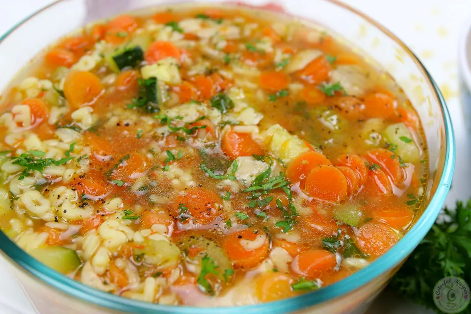Glass bowl of alphabet chicken soup with carrots, celery and parsley