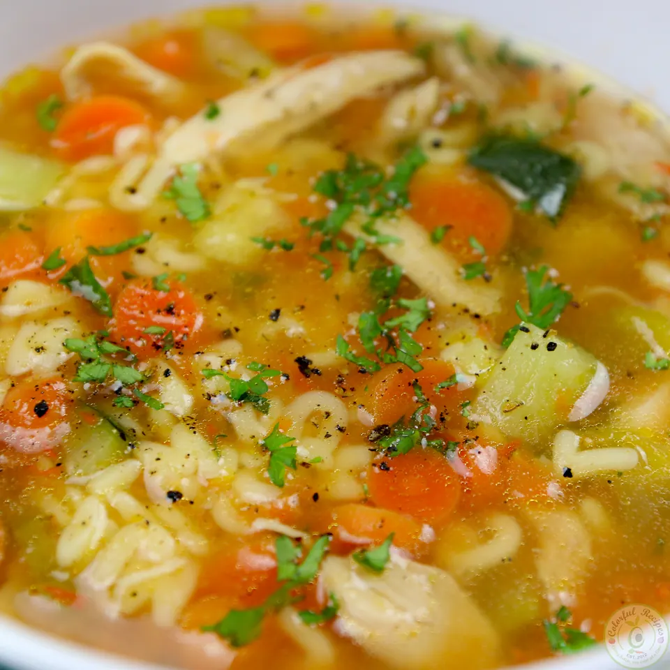 Close-up of alphabet chicken soup with shredded chicken, zucchini and parsley