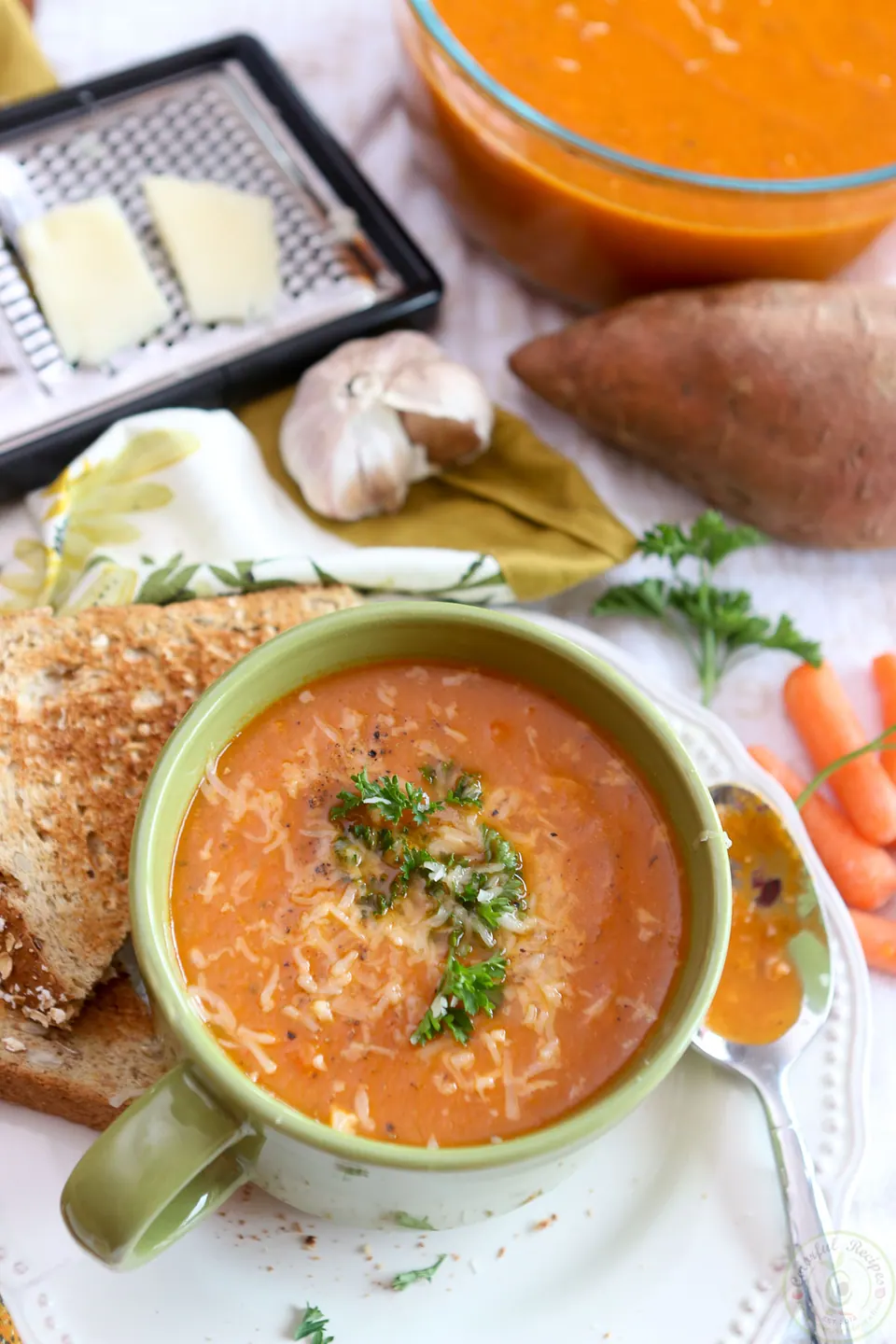 Bowl of roasted red pepper sweet potato soup topped with grated Asiago and herbs