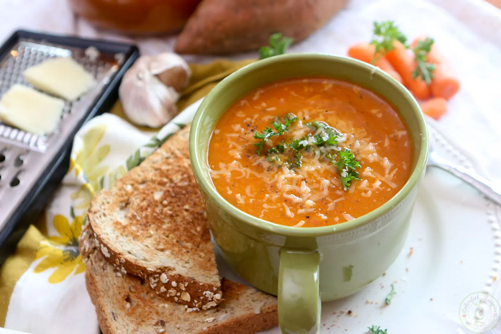 Roasted red pepper sweet potato soup in a green mug with toast and grated Asiago