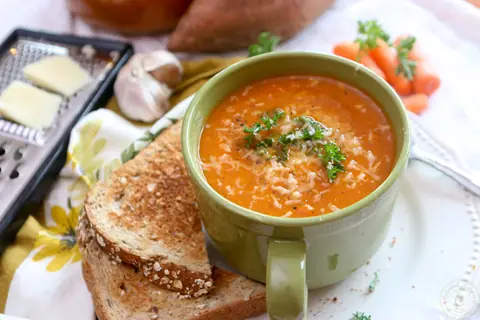 Roasted red pepper sweet potato soup in a green mug with toast and grated Asiago