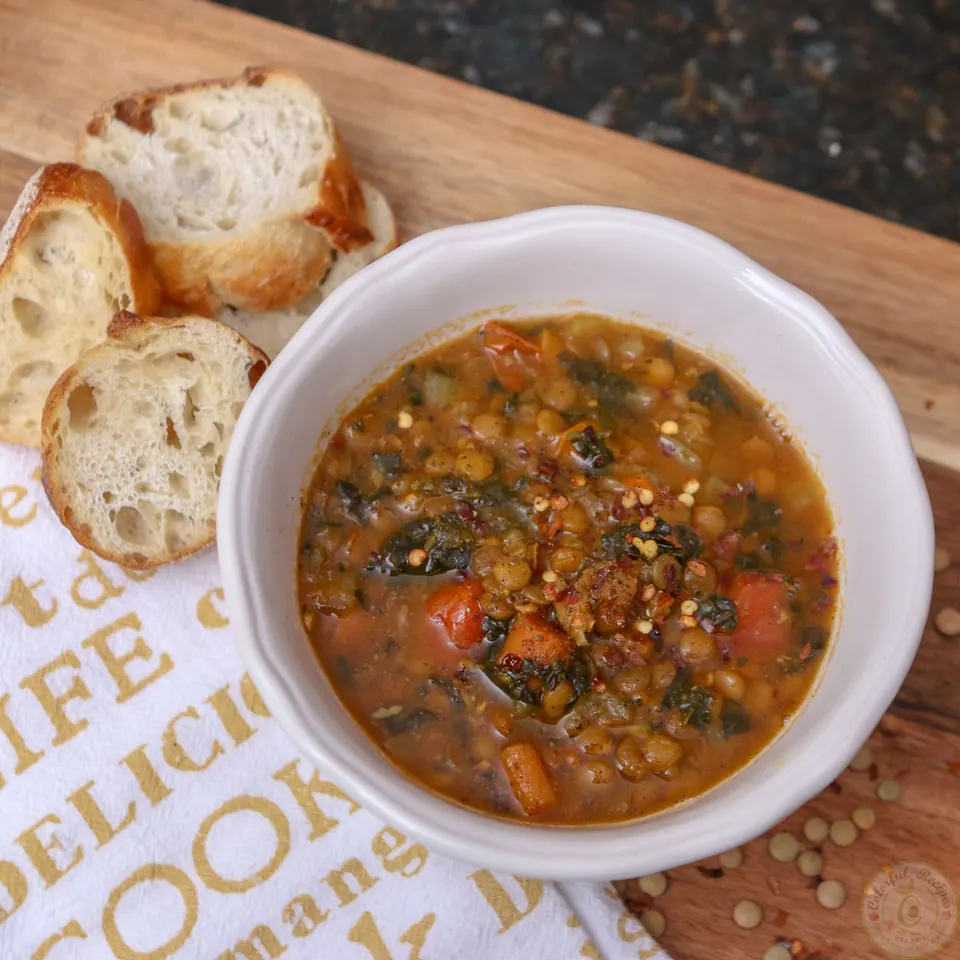 Instant Pot lentil spinach hearty soup with sliced baguette on a wooden board