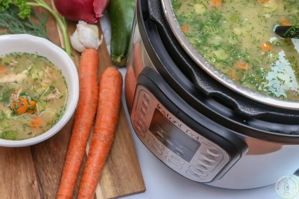 Bowl of homemade chicken soup next to the Instant Pot and fresh carrots