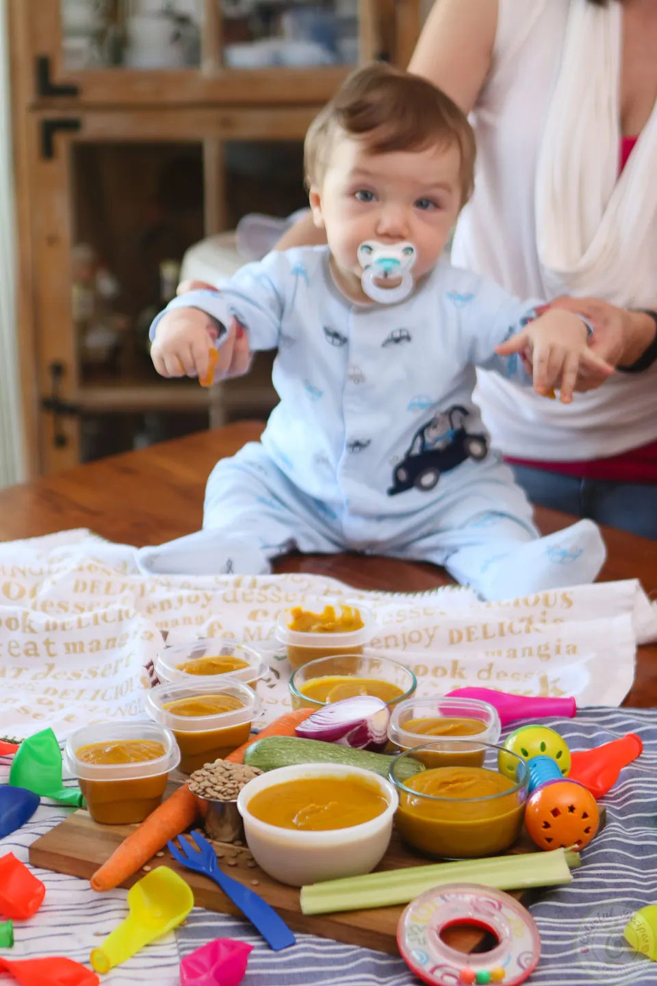 Baby sitting behind containers of homemade veggie lentil baby purée