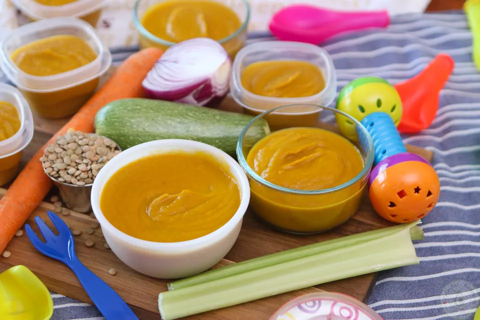 Bowl of creamy veggie lentil baby purée surrounded by fresh vegetables