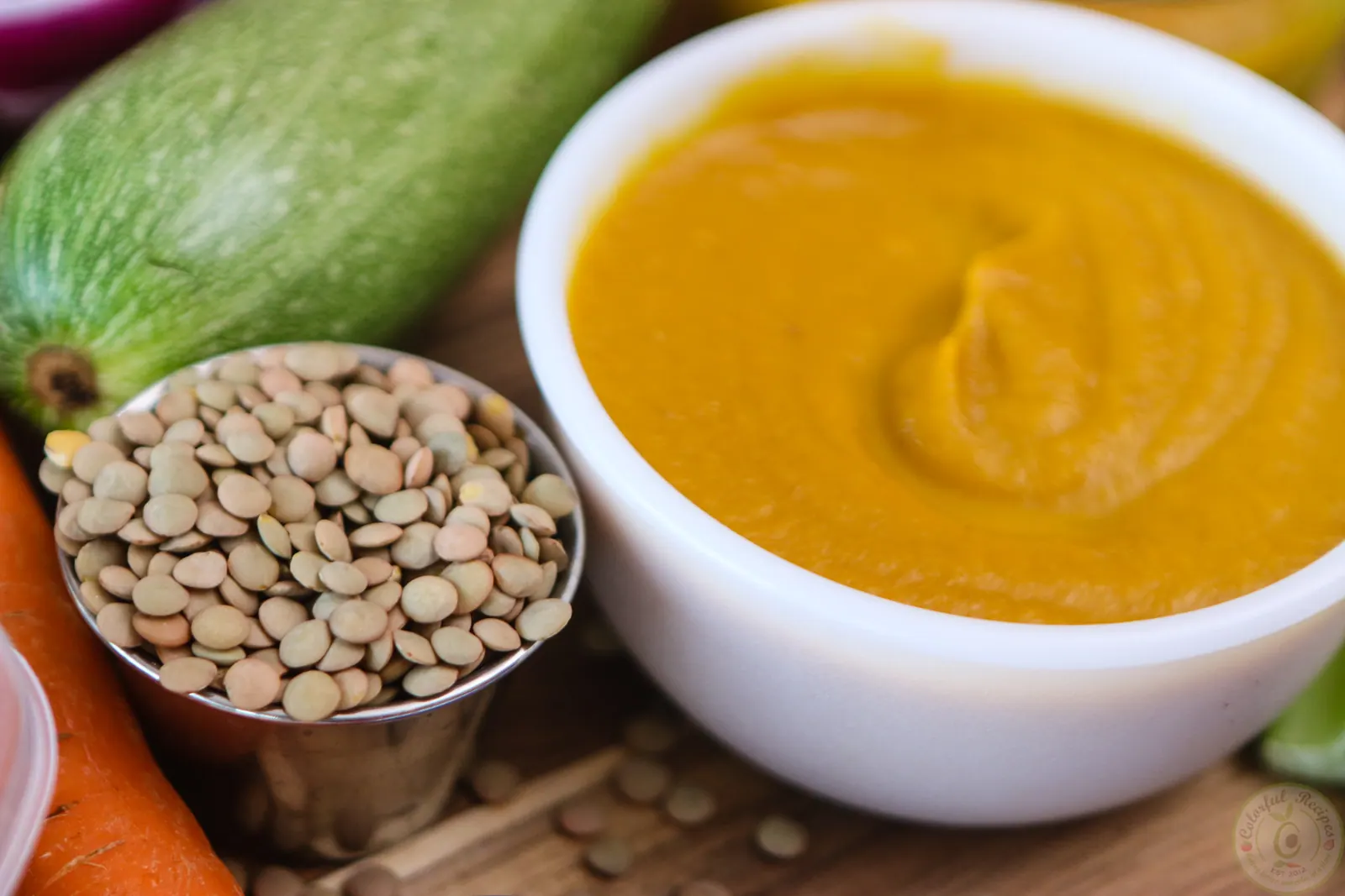 Bowl of creamy veggie lentil baby purée surrounded by fresh vegetables
