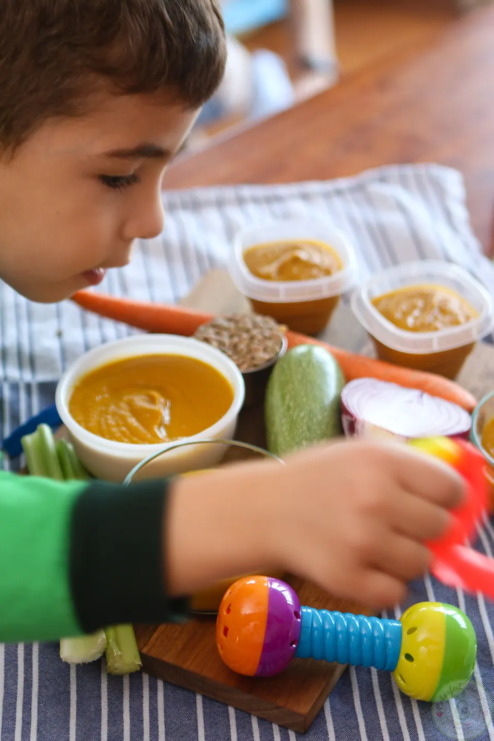 Big brother Roy decorating a table of veggie lentil baby purée with toys