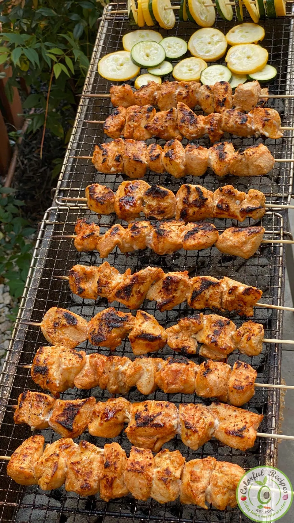 Rows of grilled chicken kabobs on an open mankal grill