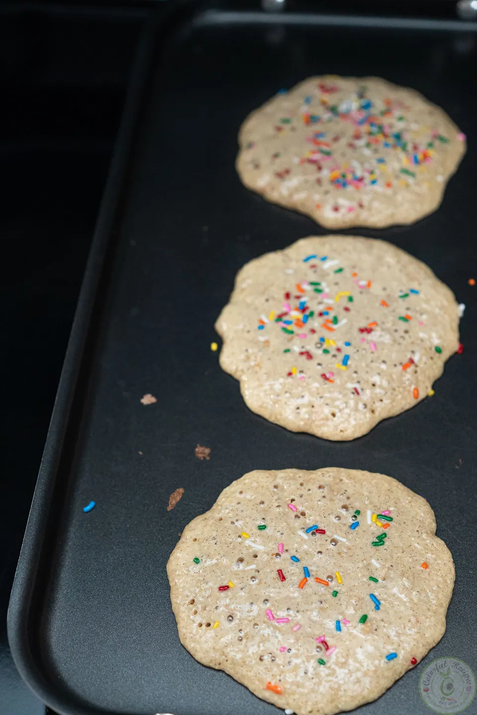 Oatmeal pancakes with colorful sprinkles cooking on a griddle