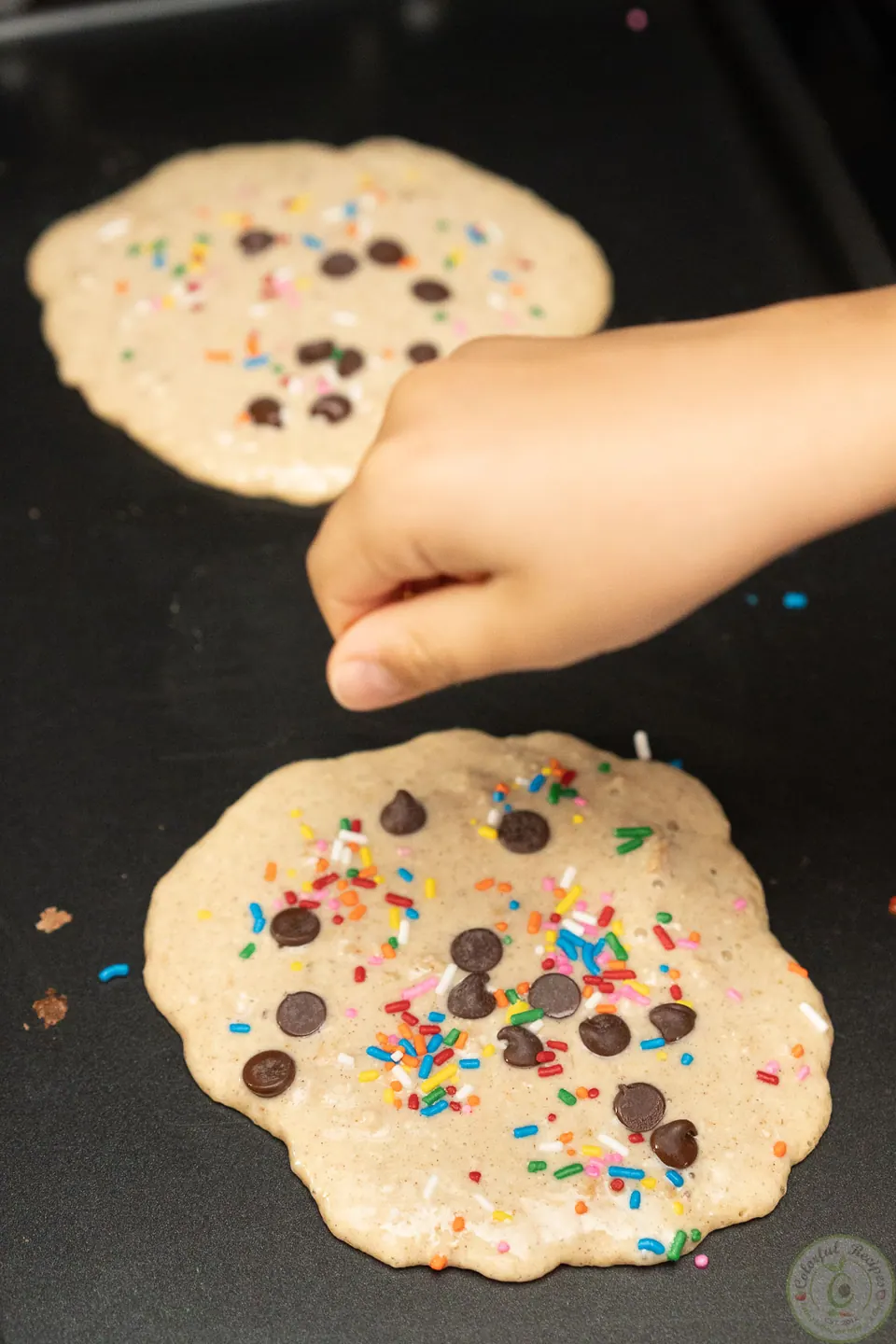 Child adding chocolate chips to oatmeal pancakes on the griddle