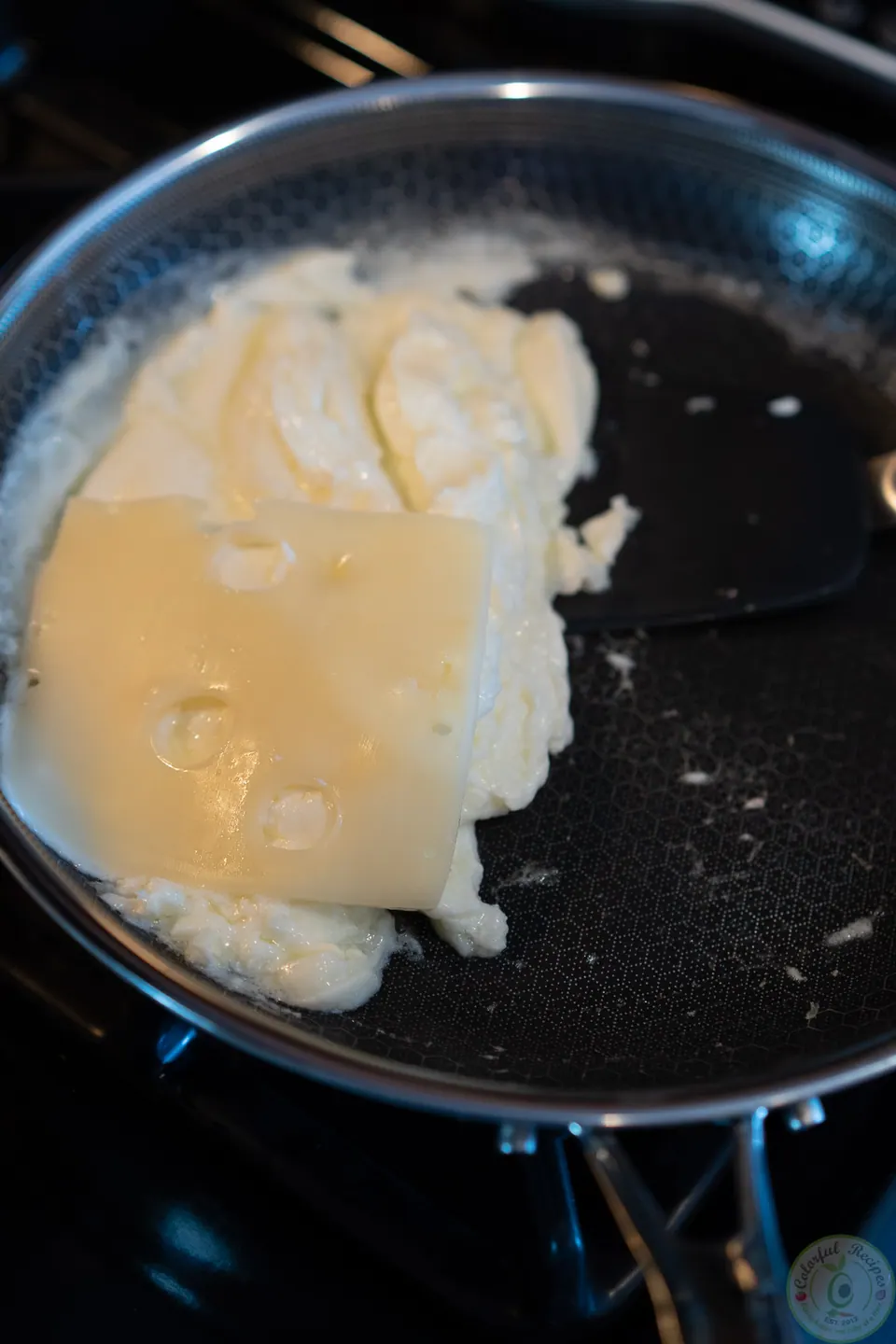 Slice of Swiss cheese softening on cooked egg whites in the pan