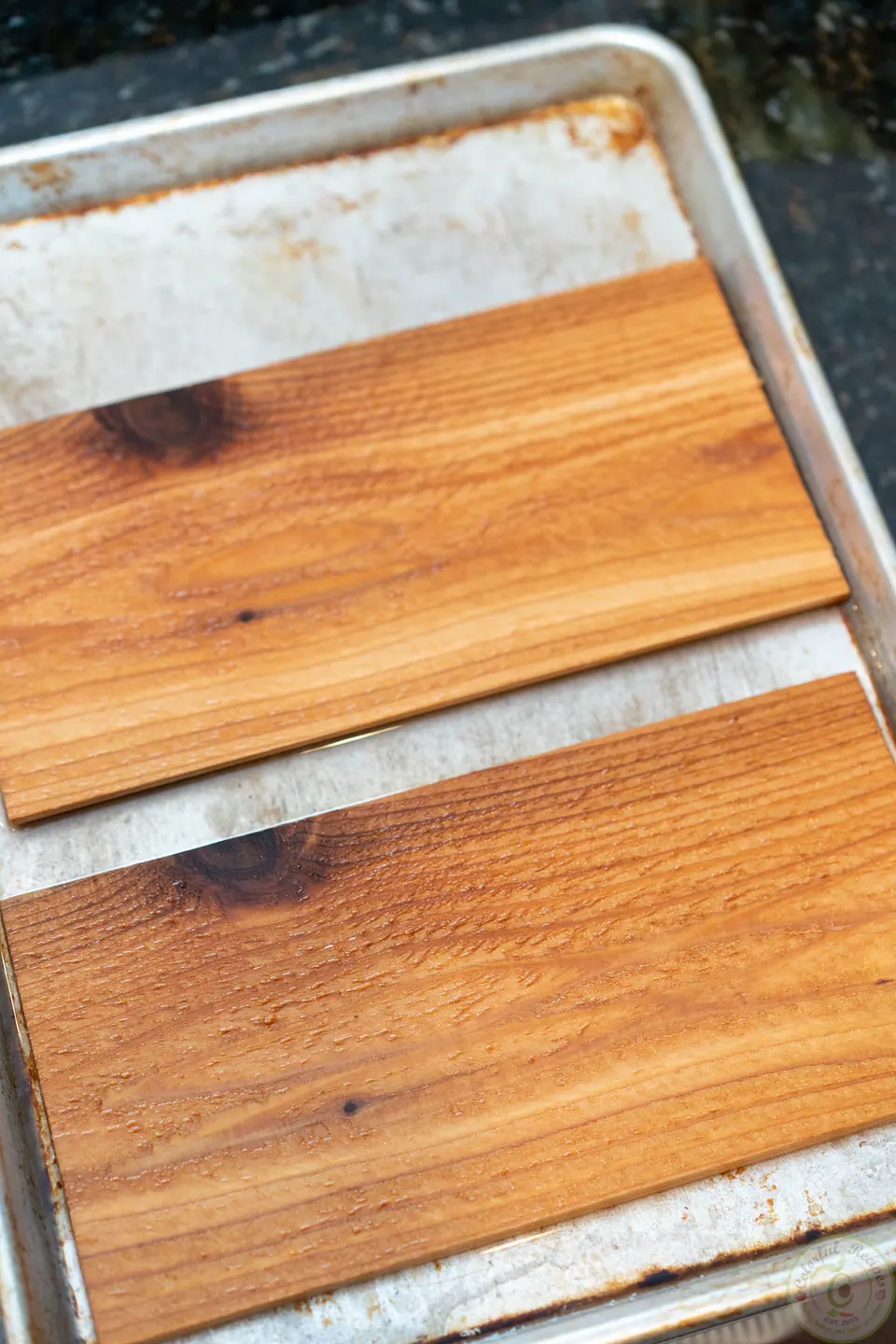 Two cedar planks soaking in a baking sheet before grilling salmon